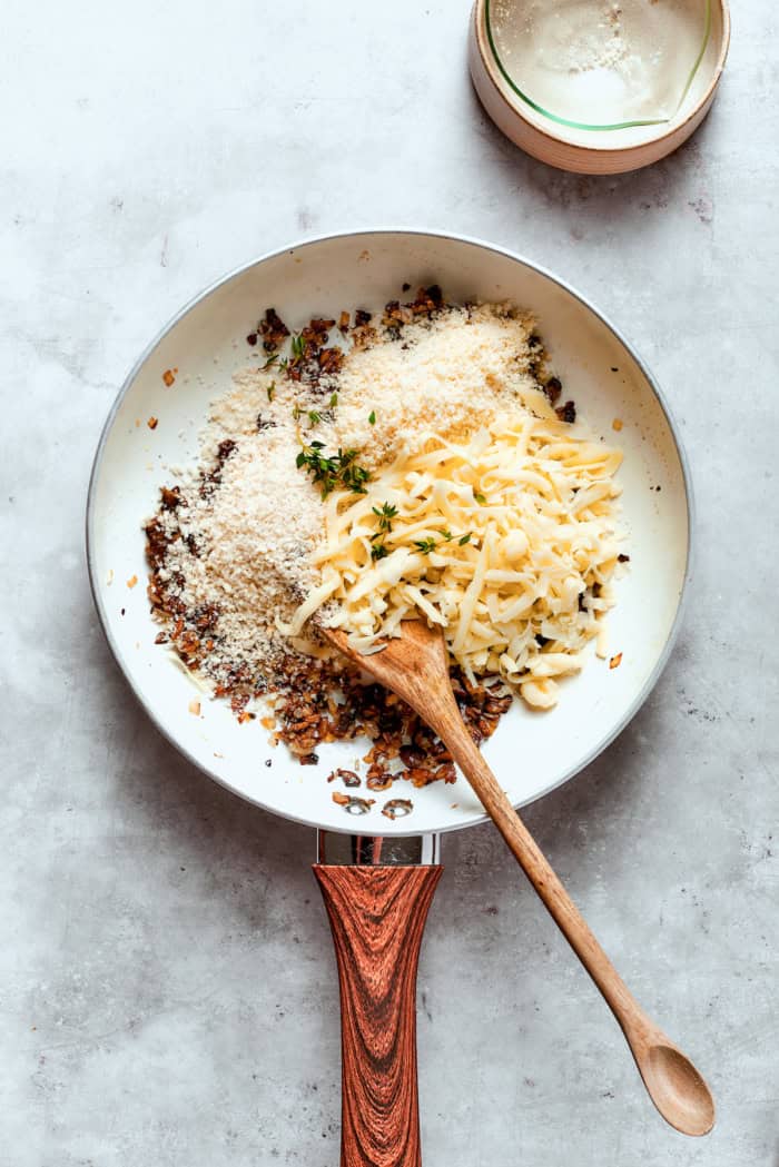 These easy Cheesy Stuffed Mushrooms are an irresistible appetizer or side dish, with lots of melty cheese and garlicky breadcrumbs. Yum! Overhead view of stuffed mushroom filling in skillet with wooden spoon