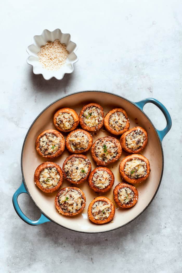 These easy Cheesy Stuffed Mushrooms are an irresistible appetizer or side dish, with lots of melty cheese and garlicky breadcrumbs. Yum! Overhead view of cheese stuffed mushrooms in skillet with bowl of Parmesan