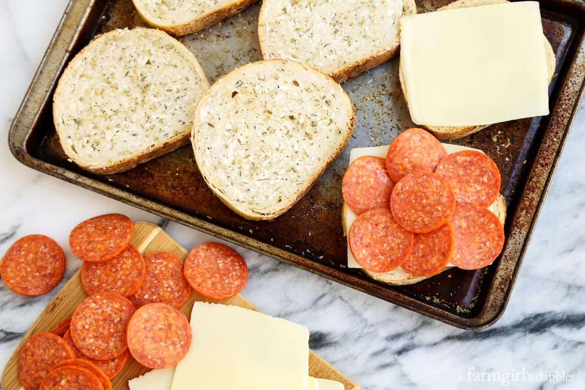 Dip this melty mozzarella-pepperoni pizza grilled cheese recipe into tomato sauce for an easy weeknight dinner that's ready in 12 minutes! Landscape photo of adding the mozzarella and pepperoni over the bread on a baking sheet.