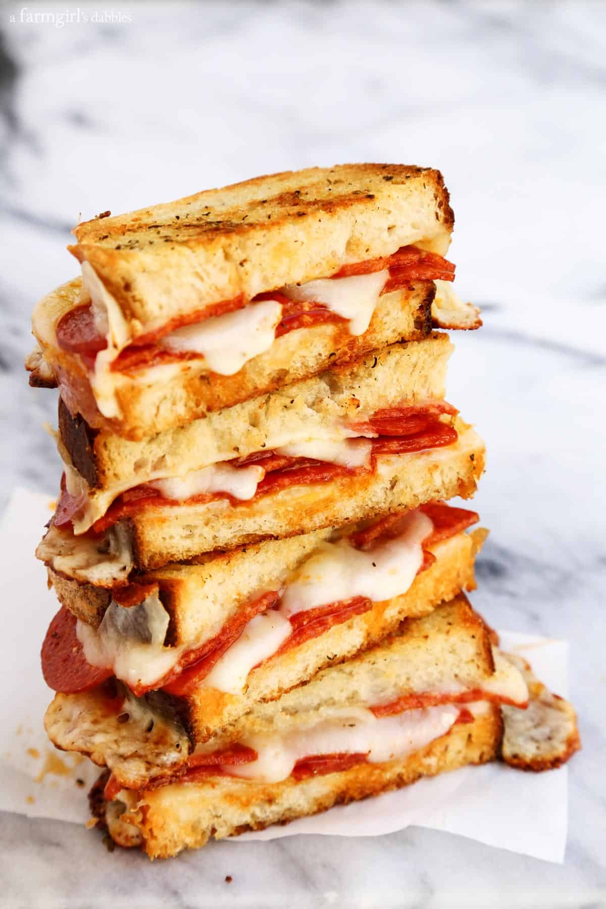 Dip this melty mozzarella-pepperoni pizza grilled cheese recipe into tomato sauce for an easy weeknight dinner that's ready in 12 minutes! A stack of pepperoni pizza grilled cheese halves.