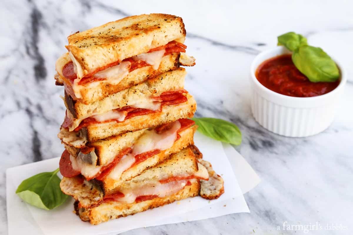 Dip this melty mozzarella-pepperoni pizza grilled cheese recipe into tomato sauce for an easy weeknight dinner that's ready in 12 minutes! Landscape photo of grilled cheese halves with salty pepperoni and sweet tomato sauce for dipping on the side.