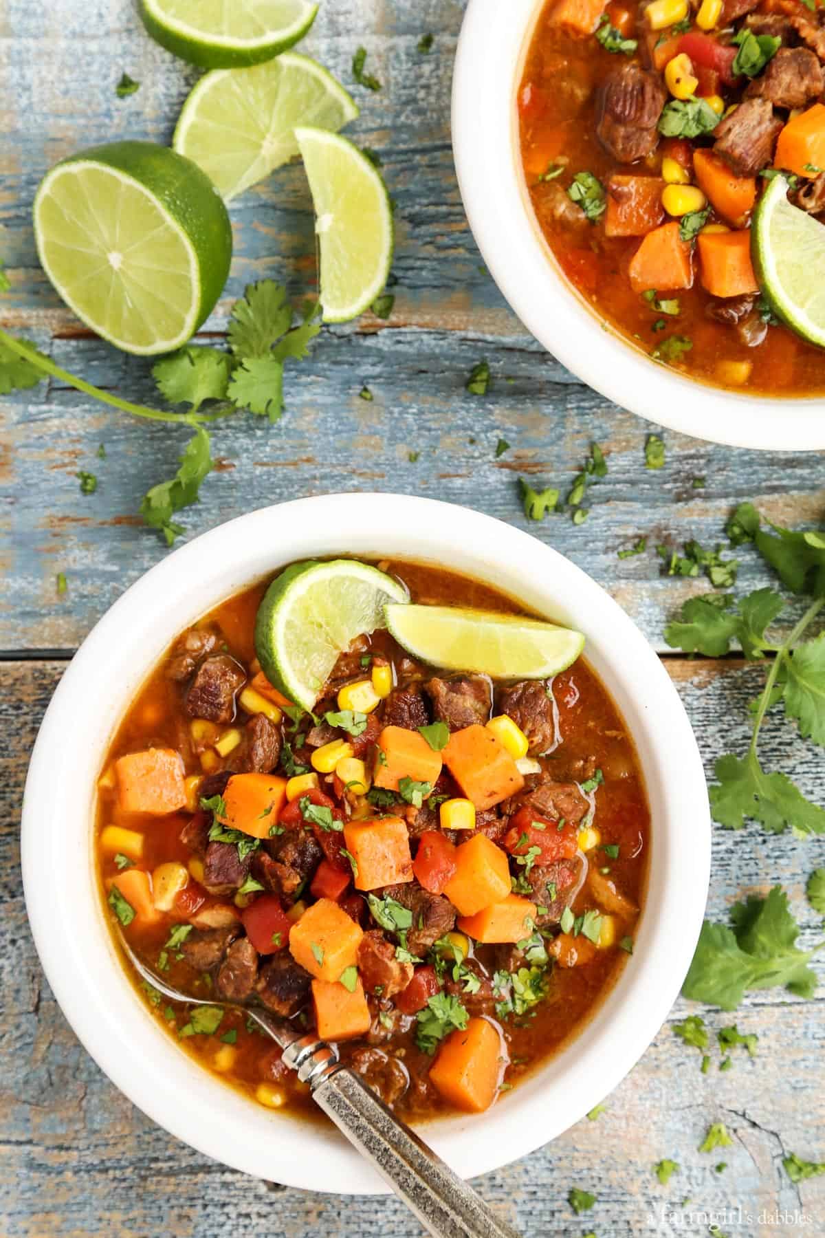 This Southwestern slow cooker beef stew with sweet potatoes combines hearty ingredients in a rich broth, brightened with a squeeze of lime! Overhead view of bowls of beef stew with sweet potatoes garnished with lime wedges.