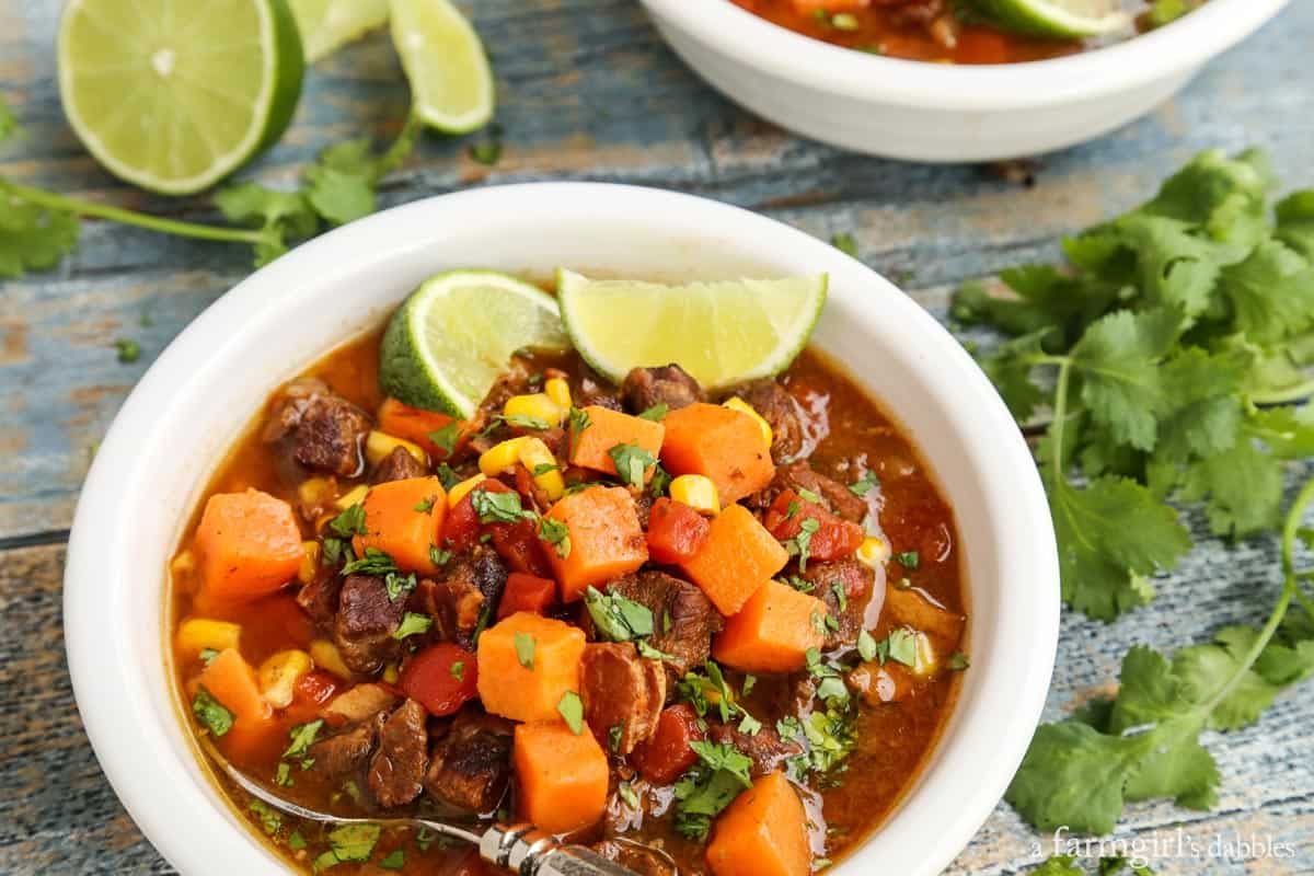 This Southwestern slow cooker beef stew with sweet potatoes combines hearty ingredients in a rich broth, brightened with a squeeze of lime! A bowl of beef stew with sweet potatoes garnished with lime wedges.