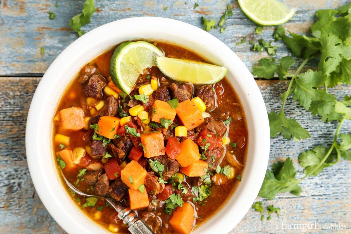 This Southwestern slow cooker beef stew with sweet potatoes combines hearty ingredients in a rich broth, brightened with a squeeze of lime! Overhead view of a bowl of beef stew with sweet potatoes garnished with lime wedges.