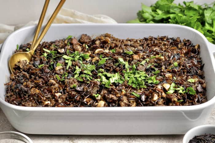 This creamy Wild Rice Casserole with sausage and mushrooms is deeply savory, hearty, and perfect for cozy dinners and holiday celebrations! Baking dish of wild rice casserole with parsley for garnish.