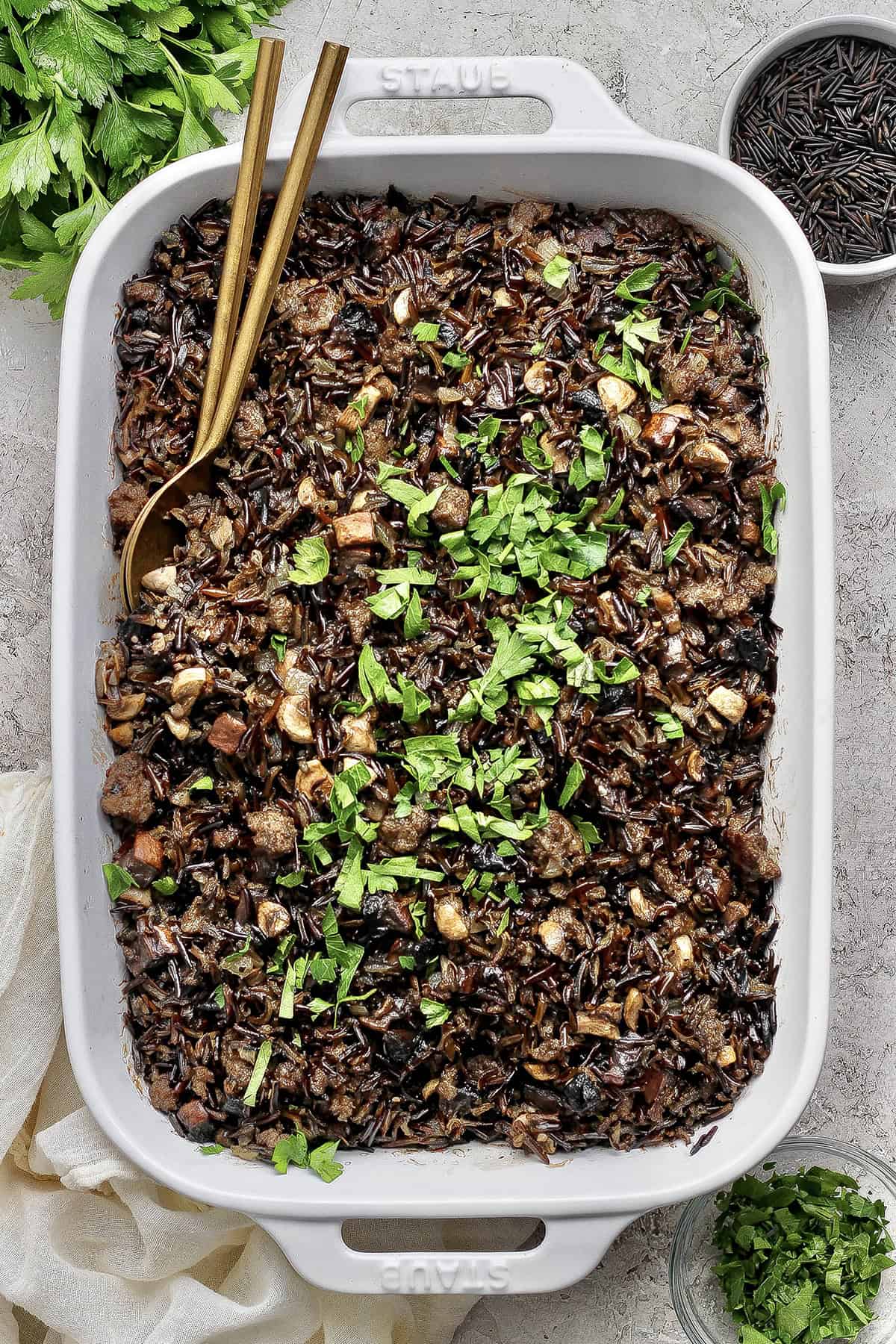 This creamy Wild Rice Casserole with sausage and mushrooms is deeply savory, hearty, and perfect for cozy dinners and holiday celebrations! Creamy wild rice casserole in baking dish with two spoons for serving.