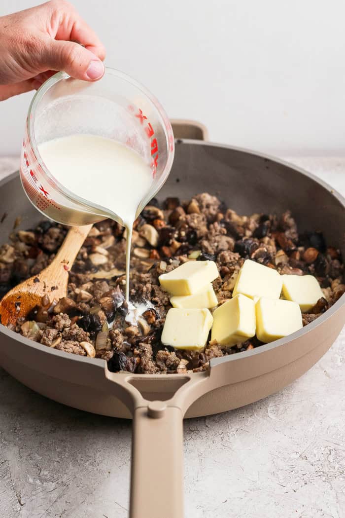 This creamy Wild Rice Casserole with sausage and mushrooms is deeply savory, hearty, and perfect for cozy dinners and holiday celebrations! Pouring cream into wild rice casserole with cubes of butter.