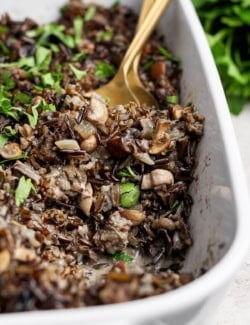 Spoon digging into wild rice casserole with mushrooms and sausage.