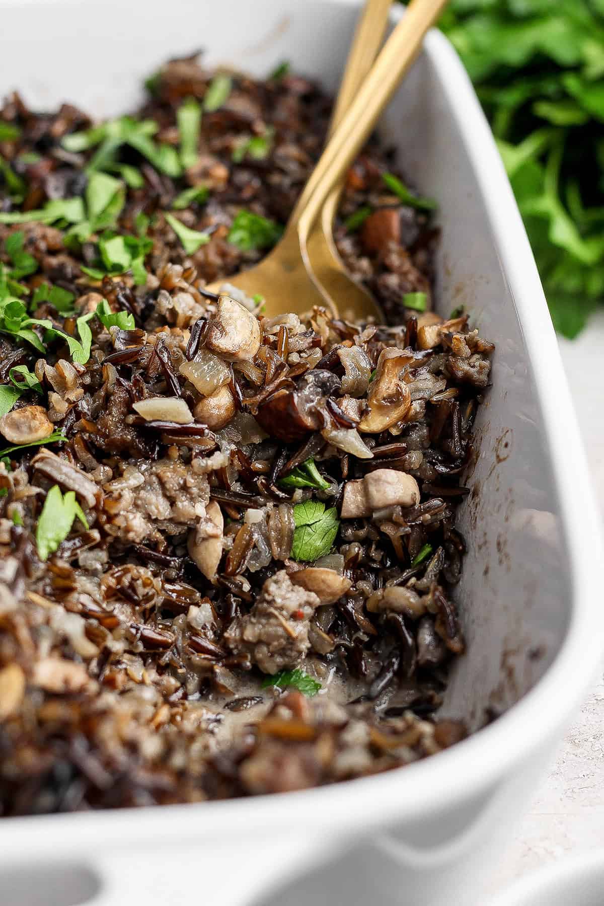 This creamy Wild Rice Casserole with sausage and mushrooms is deeply savory, hearty, and perfect for cozy dinners and holiday celebrations! Spoon digging into wild rice casserole with mushrooms and sausage.