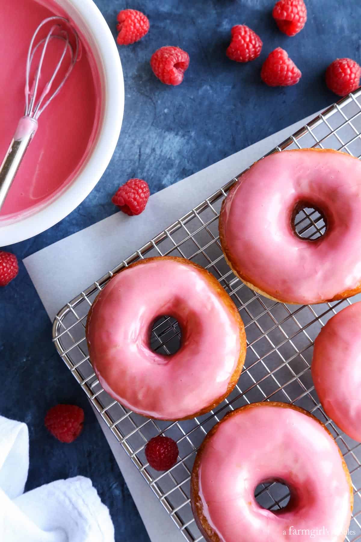 This golden, vanilla-raspberry donuts recipe with sweet lemon glaze is a yummy homemade gift for Valentine's Day. Glazed donuts on a wire rack.