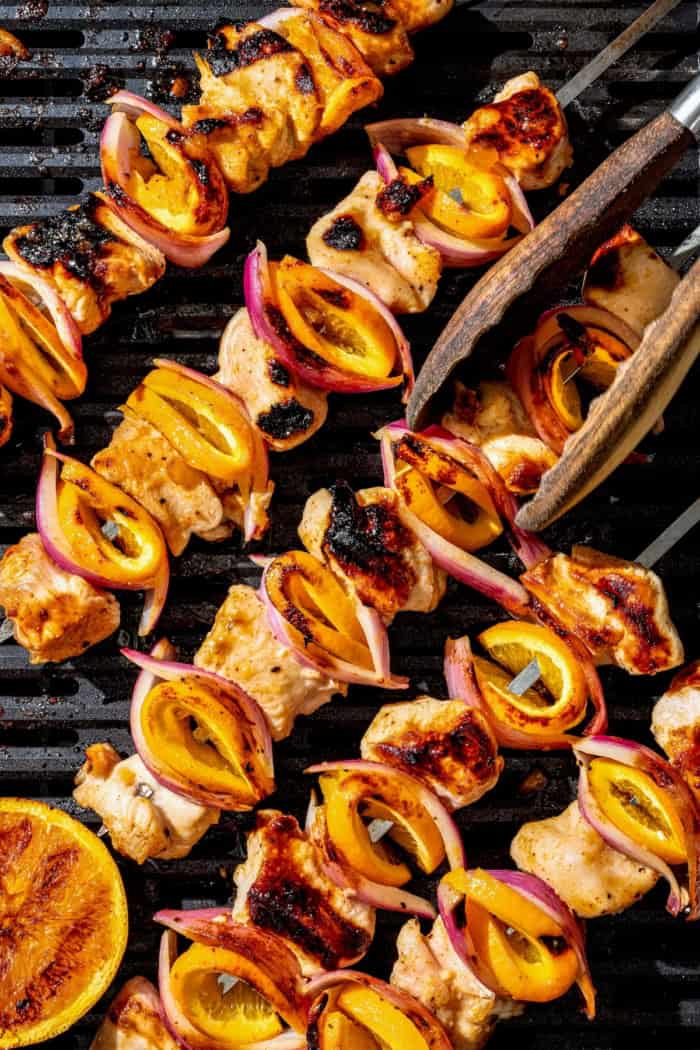 Bold, smoky chipotle meets the sweet flavor of orange in these easy Turkey Kabobs. This recipe is a summer staple in my home! Overhead view of grilled chipotle orange turkey kabobs on grill, being turned with tongs