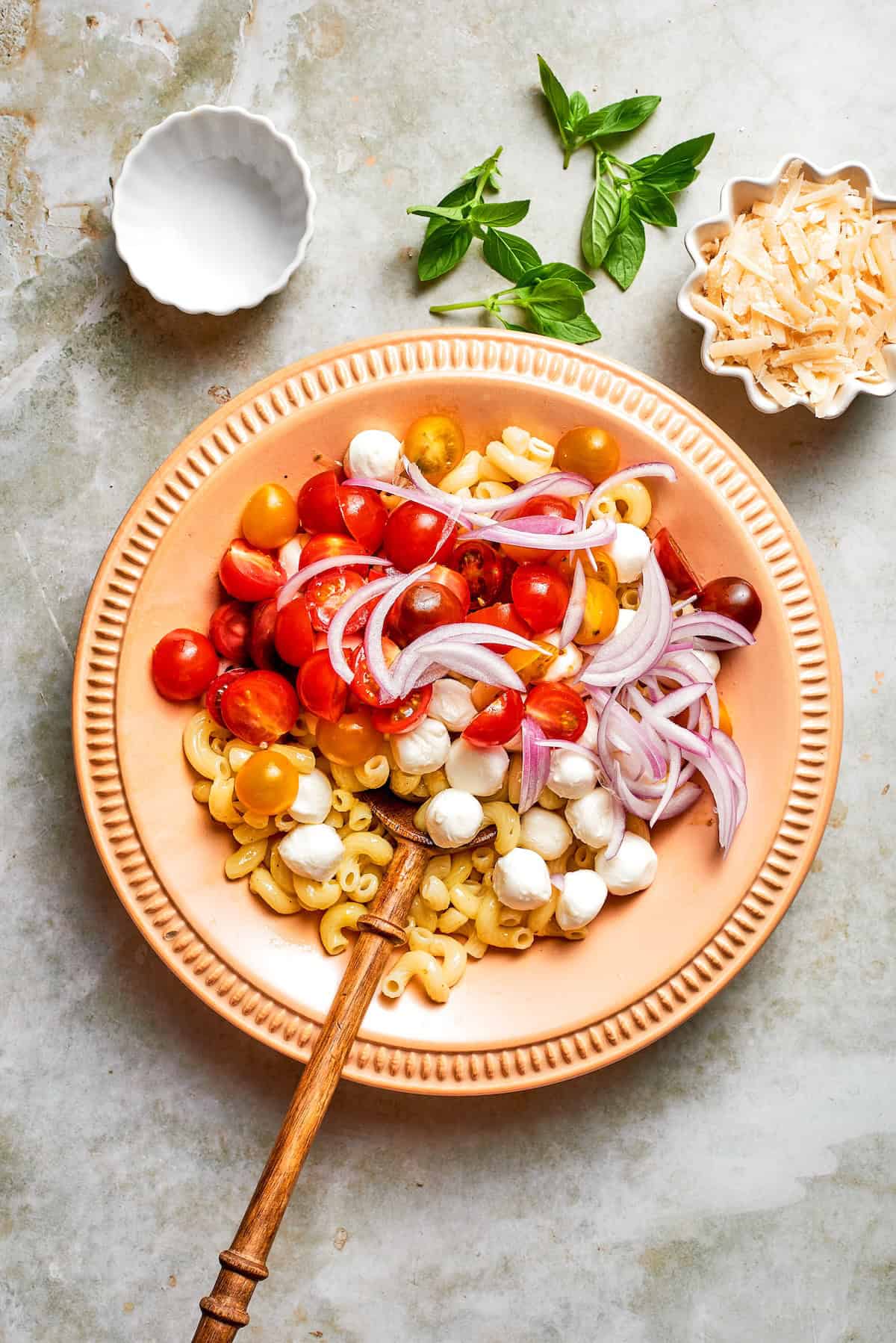 Onions, tomatoes, and mozzarella added to bowl of pasta.