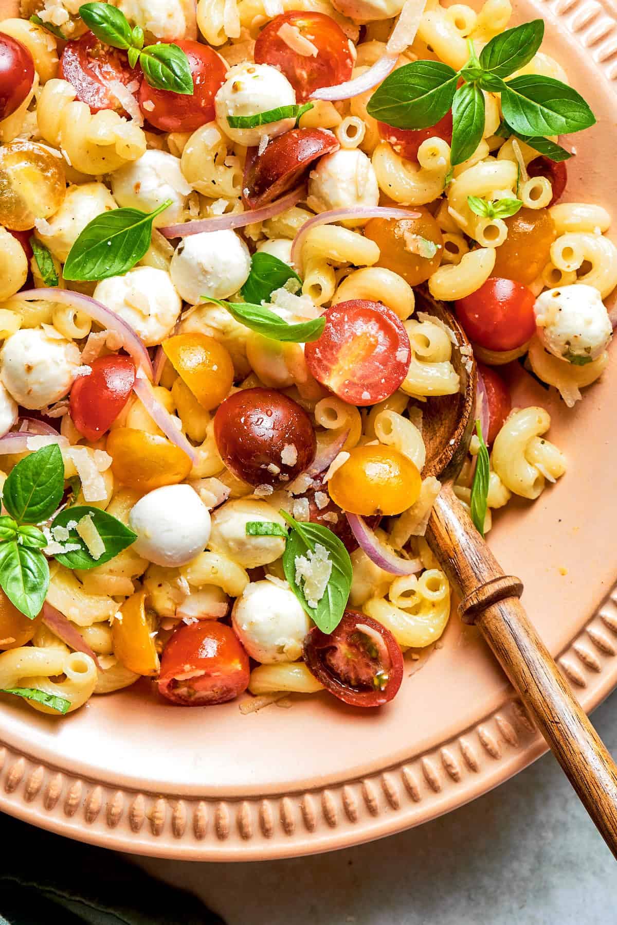 Caprese pasta salad in bowl with wooden spoon.
