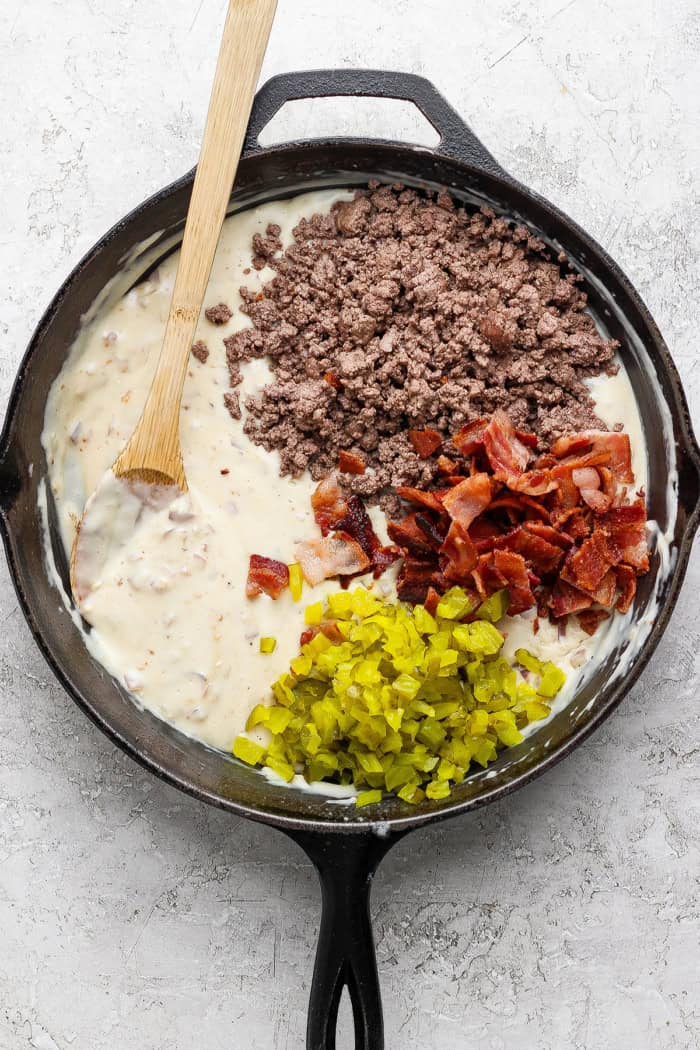 Crispy tater tots, ground beef, smoky bacon and cheese make this bacon cheeseburger tater tot casserole taste like a burger in hot dish form! Beef, bacon, and pickles added to skillet of creamy sauce.