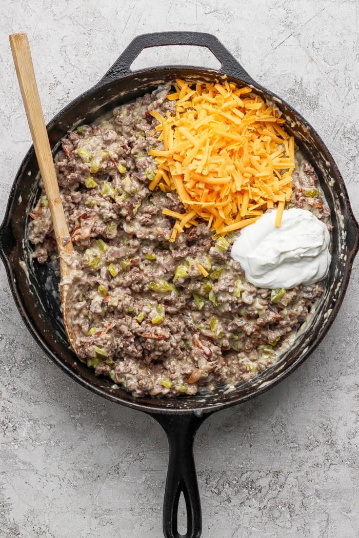 Crispy tater tots, ground beef, smoky bacon and cheese make this bacon cheeseburger tater tot casserole taste like a burger in hot dish form! Sour cream and cheddar added to skillet of creamy ground beef.