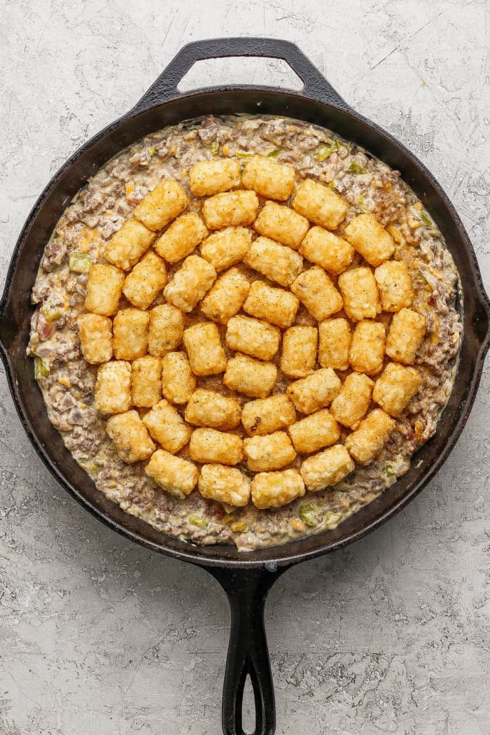 Crispy tater tots, ground beef, smoky bacon and cheese make this bacon cheeseburger tater tot casserole taste like a burger in hot dish form! Bacon cheeseburger casserole in skillet before baking.