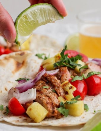 Squeezing lime juice onto grilled pork and pineapple taco