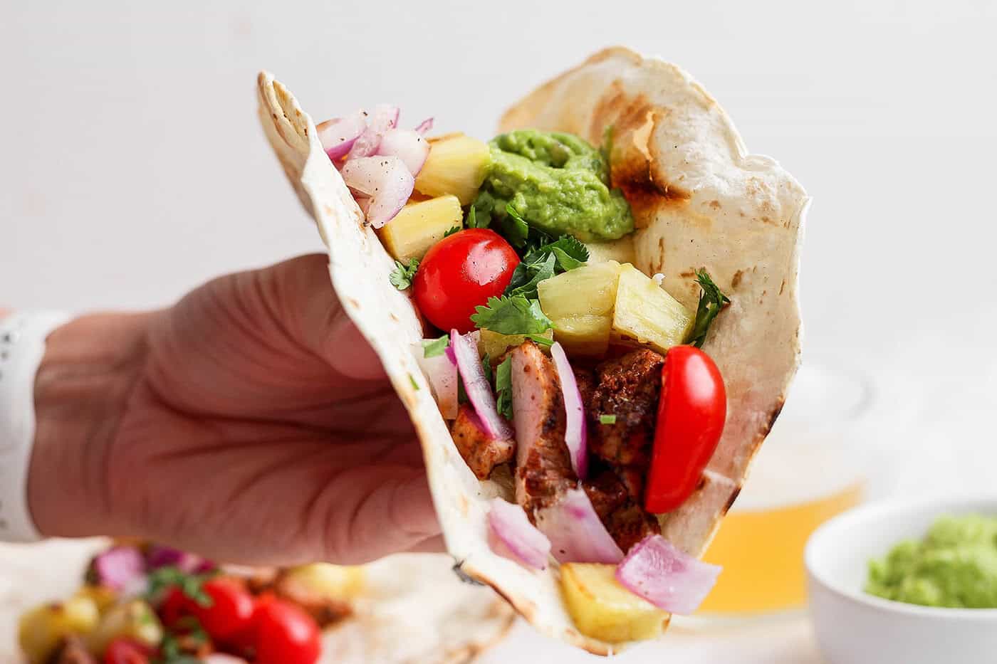 This Grilled Pork and Pineapple Tacos recipe a much easier twist on tacos al pastor. It promises to be your next taco night hit! Hand holding grilled pork and pineapple taco