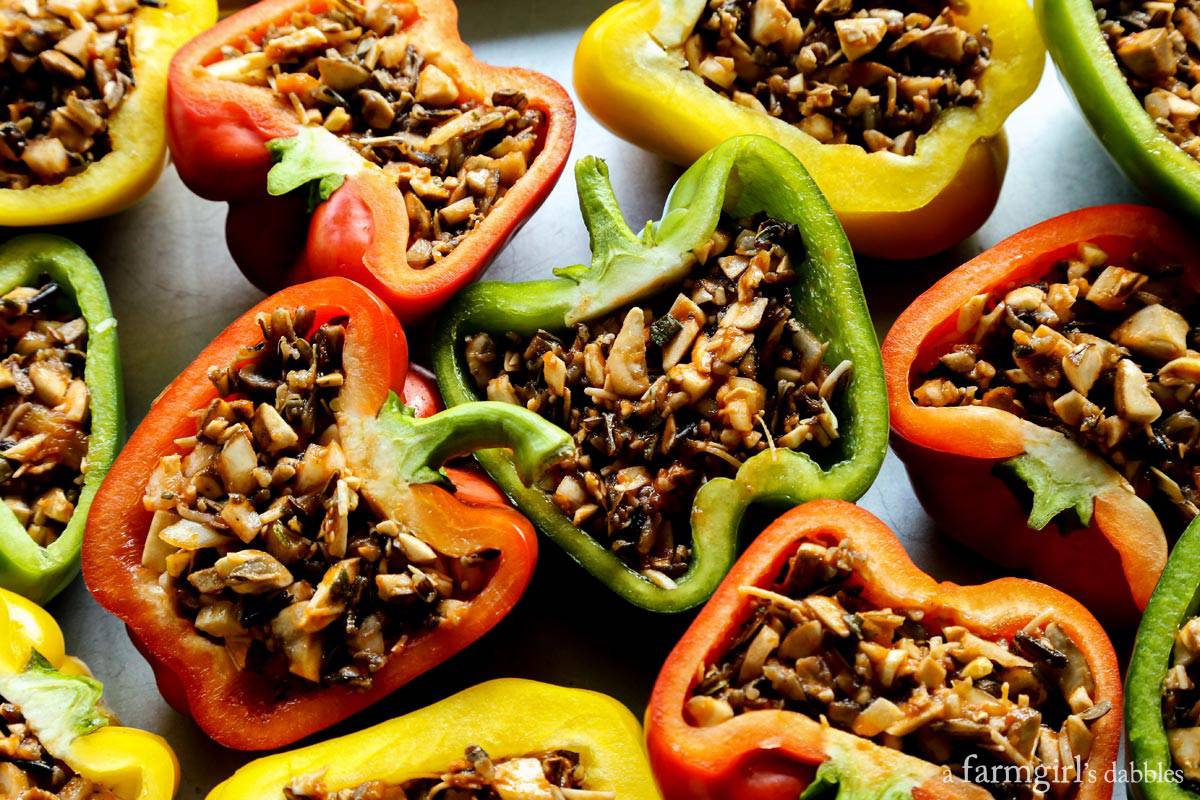 This Stuffed Peppers with Rice recipe is packed with an irresistible blend of wild rice, zesty tomato sauce, salty cheese, and vegetables. Stuffed peppers with rice are shown on a rimmed pan before being cooked.