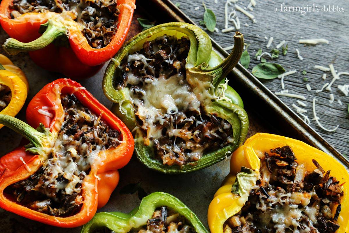 This Stuffed Peppers with Rice recipe is packed with an irresistible blend of wild rice, zesty tomato sauce, salty cheese, and vegetables. Stuffed peppers with rice and cheese and herbs on a baking pan.