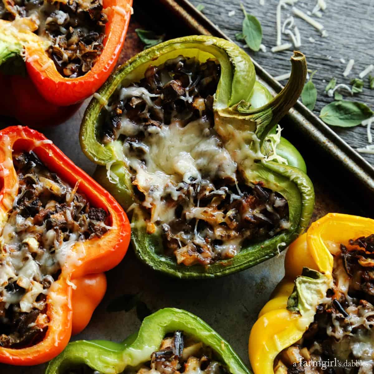 This Stuffed Peppers with Rice recipe is packed with an irresistible blend of wild rice, zesty tomato sauce, salty cheese, and vegetables. Stuffed peppers with rice are shown on a rimmed pan.