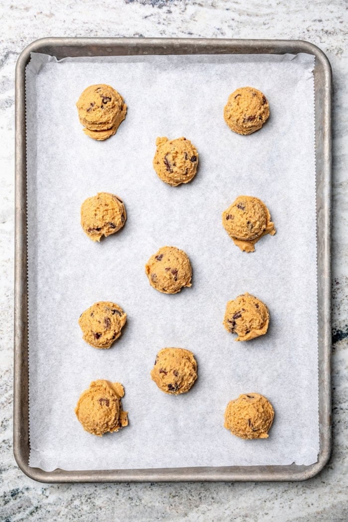 These soft, chewy peanut butter chocolate chip cookies are extra wonderful with three kinds of chocolate, plus a sprinkle of sea salt! Balls of peanut butter chocolate chip cookie dough on sheet pan.