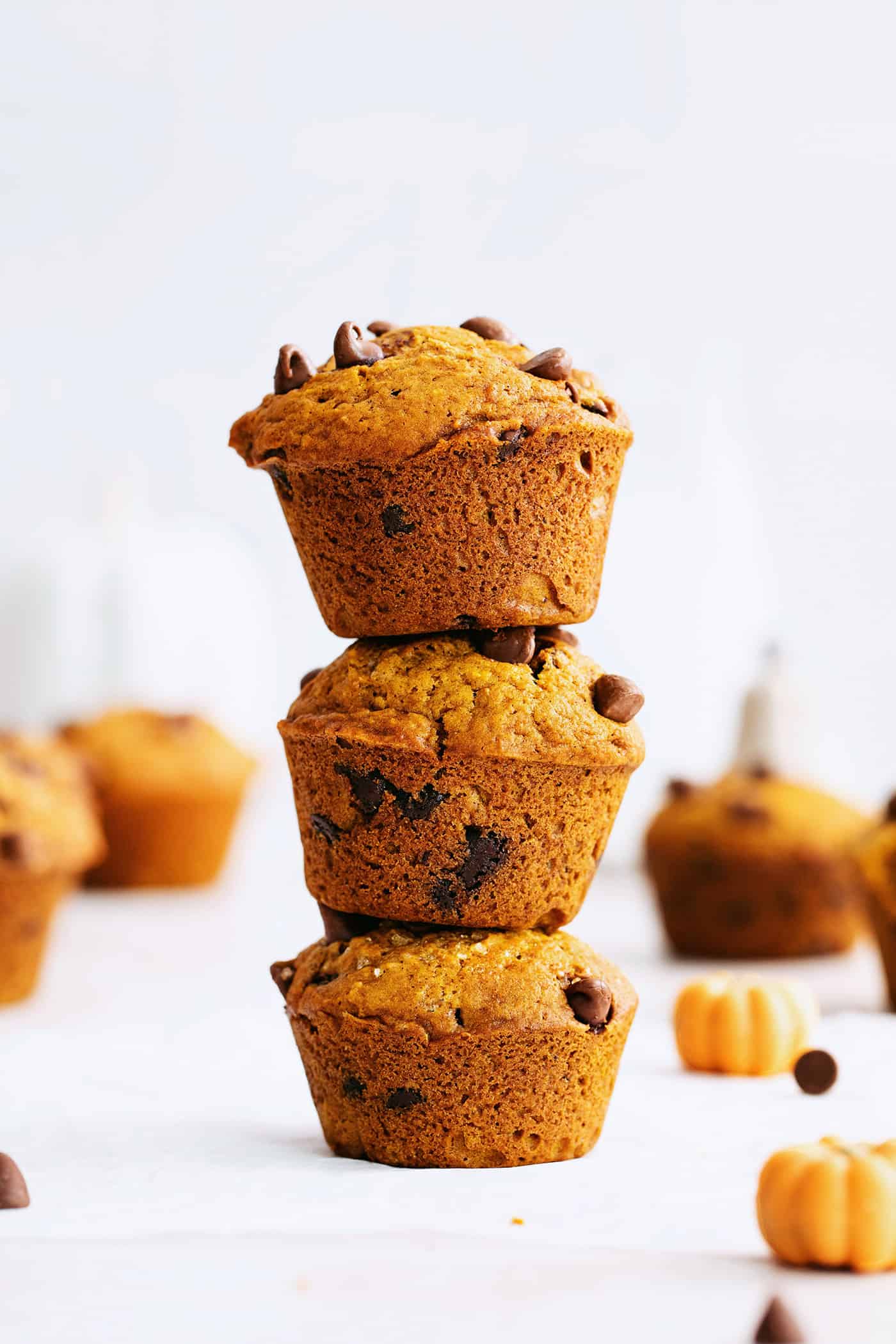 This fluffy pumpkin chocolate chip muffins recipe with warm spices will be your go-to baking project for a lovely fall brunch. Three stacked muffins on the counter.