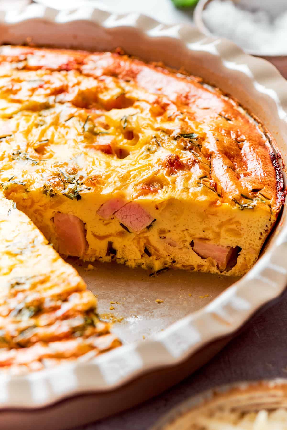 This cheesy crustless quiche recipe with ham, tangy Dijon, and chives is an easy baked dish for the holidays. Side-shot of the fluffy, baked quiche in the pie dish.