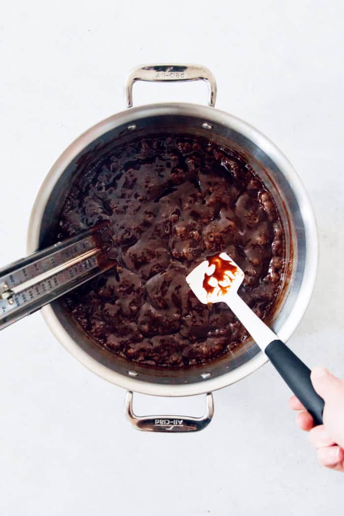 Using a candy thermometer to read the caramel's temperature.
