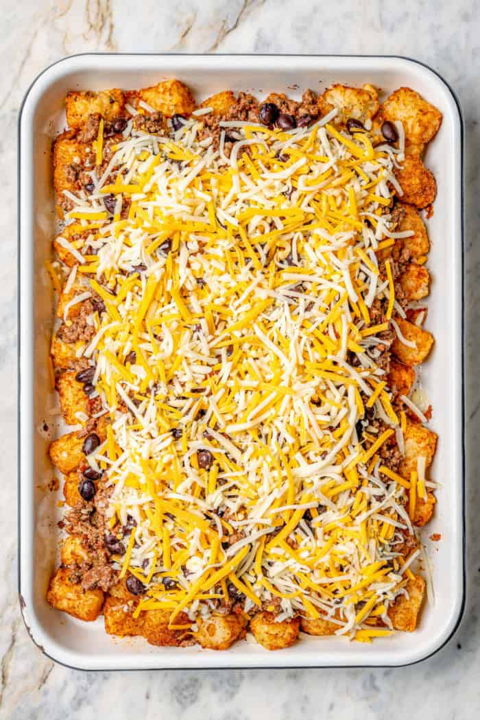 Overhead view of ground beef, beans, and cheese added to totchos