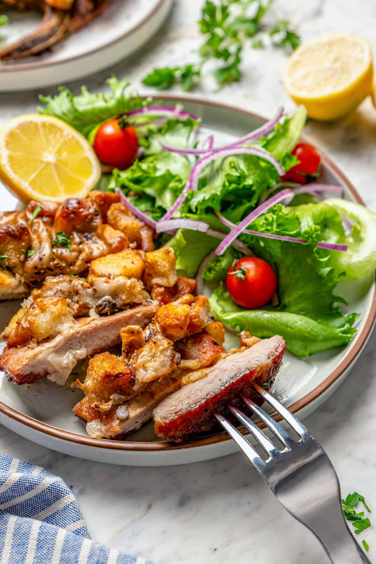Close-up of a slice of juicy pork chop on a fork, with a side of fresh salad on the dinner plate.