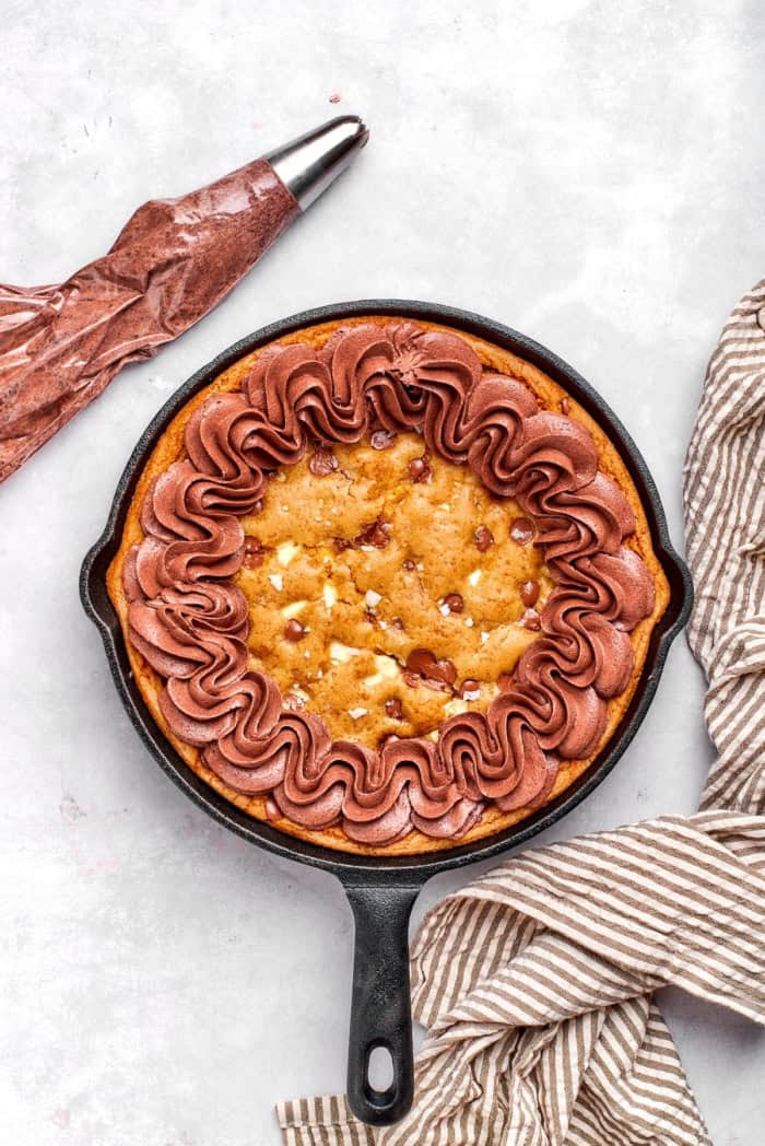Nutty brown butter, flaky sea salt and fluffy buttercream make this chewy chocolate chip skillet cookie worthy of a celebration. So easy too! Chocolate buttercream piped onto chocolate chip cookie in cast iron skillet.