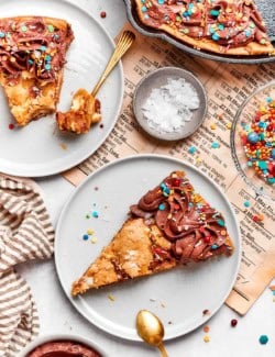 Two slices of chocolate chip skillet cookie on two plates with spoons.