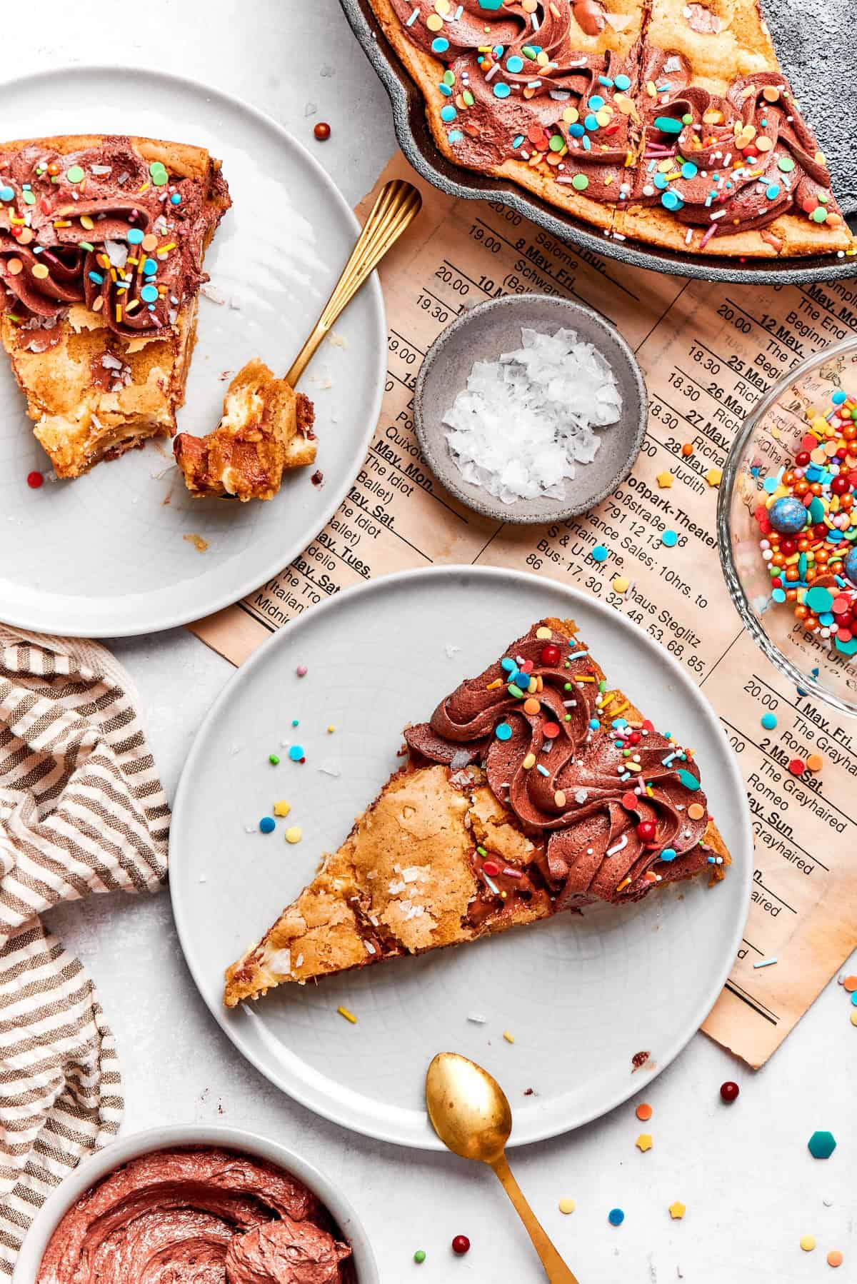 Nutty brown butter, flaky sea salt and fluffy buttercream make this chewy chocolate chip skillet cookie worthy of a celebration. So easy too! Two slices of chocolate chip skillet cookie on two plates with spoons.