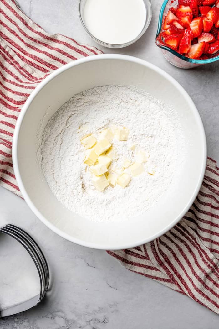 These homemade Strawberry Scones are buttery and golden, and studded with fresh berries. A drizzle of vanilla glaze is the perfect finish! Overhead view of cubed butter added to bowl of dry ingredients for scones