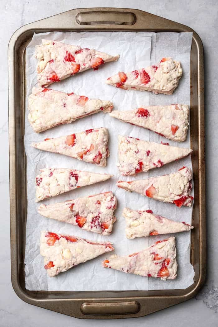 These homemade Strawberry Scones are buttery and golden, and studded with fresh berries. A drizzle of vanilla glaze is the perfect finish! Overhead view of strawberry scones on baking sheet