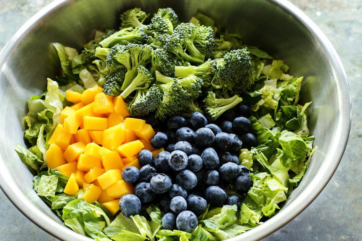 a bowl of lettuce, broccoli, blueberries, and mango