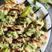 Overhead view of grilled chicken skewers on platter with green curry yogurt sauce