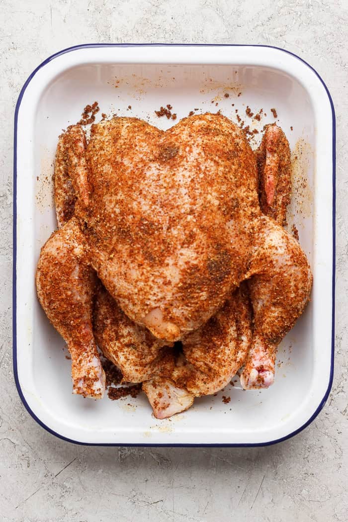 This easy Beer Can Chicken Recipe guarantees moist meat and crispy, flavorful skin. It’s our go-to recipe for a grilled whole chicken! Overhead view of seasoned whole chicken in pan