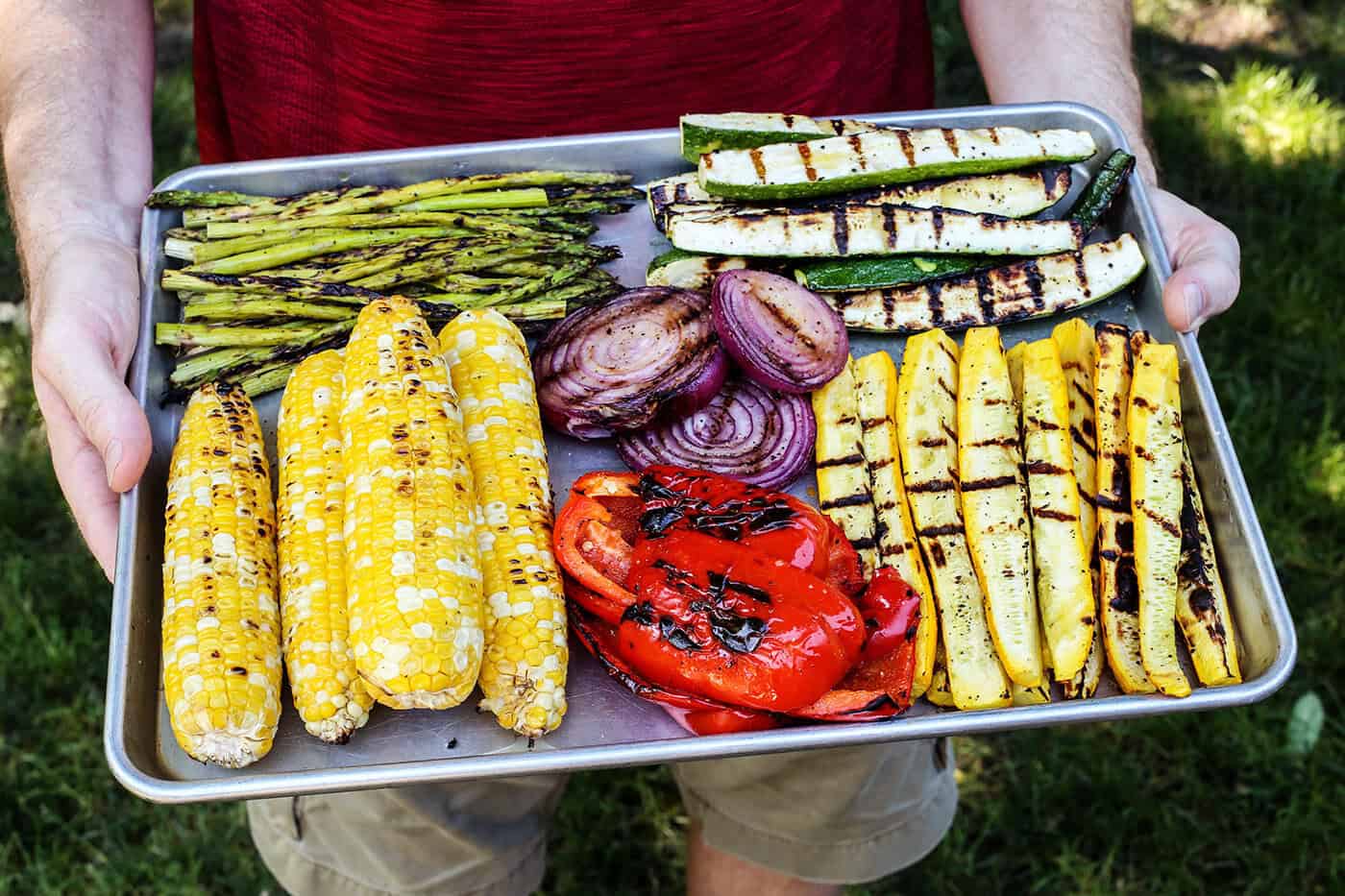 This Grilled Vegetable Salad recipe features smoky veggies, a bright lemon vinaigrette, and blue cheese (or shaved Parmesan). So flavorful! Hands holding pan of grilled vegetables