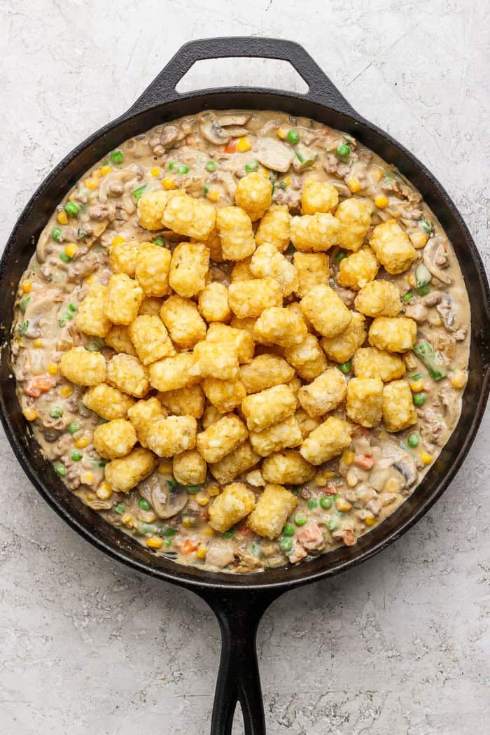 My easy made-from-scratch Tater Tot Hotdish is classic Minnesota comfort food — but fear not, I also share a canned soup version too! Overhead view of tater tot hotdish in cast iron skillet before baking
