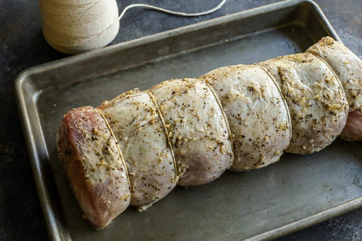 This pork loin roast recipe is juicy and tender, slathered with a savory mustard mixture and oven-roasted for a satisfying, easy pork dinner. Pork loin roast tied with kitchen twine on a baking sheet.