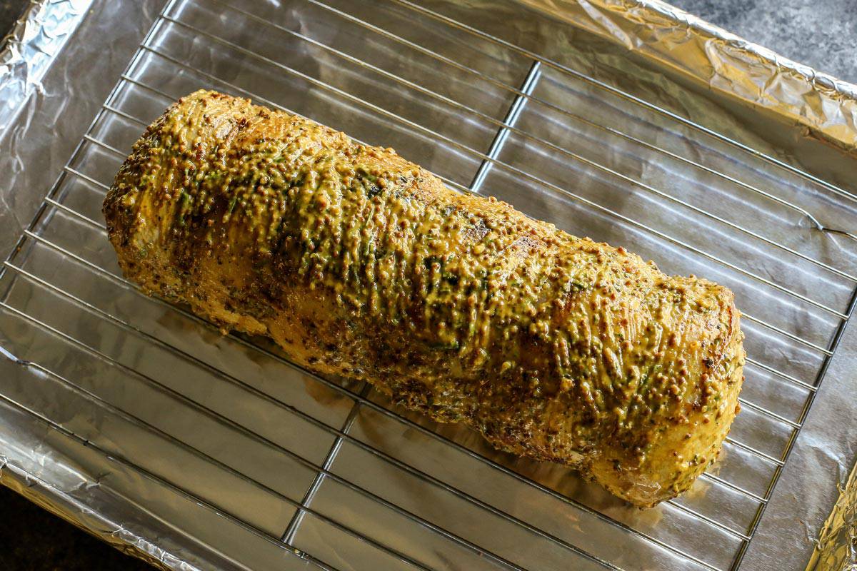 This pork loin roast recipe is juicy and tender, slathered with a savory mustard mixture and oven-roasted for a satisfying, easy pork dinner. Overhead view of a pork loin slathered with mustard sauce on a roasting rack.