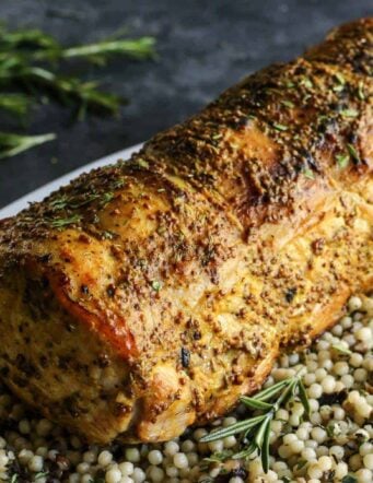 A whole pork loin roast served over a bed of pearl couscous on a plate.