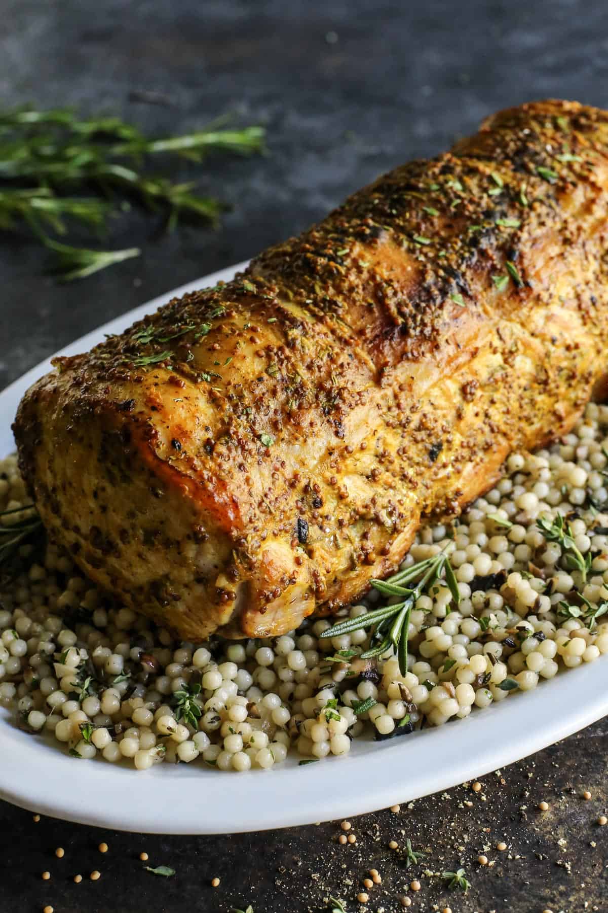 This pork loin roast recipe is juicy and tender, slathered with a savory mustard mixture and oven-roasted for a satisfying, easy pork dinner. A whole pork loin roast served over a bed of pearl couscous on a plate.