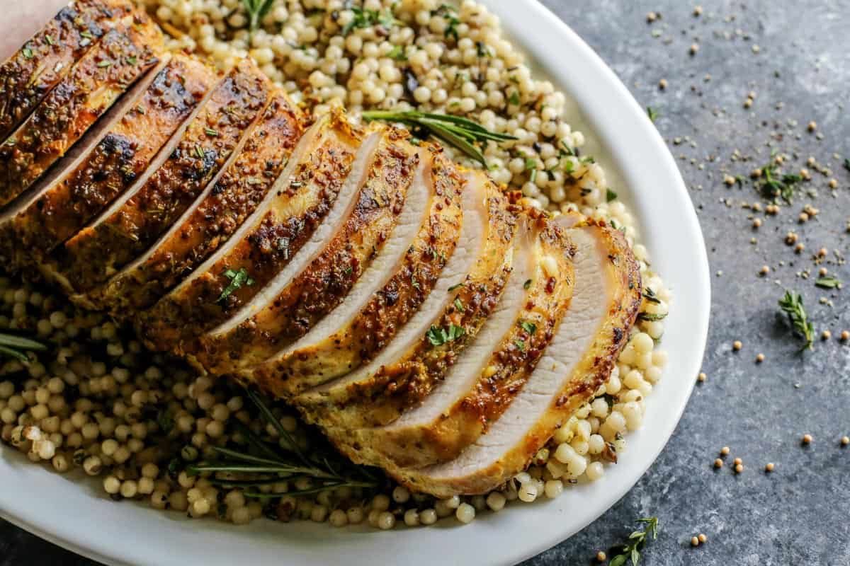 This pork loin roast recipe is juicy and tender, slathered with a savory mustard mixture and oven-roasted for a satisfying, easy pork dinner. Overhead view of sliced mustard pork loin roast over a bed of pearl couscous.