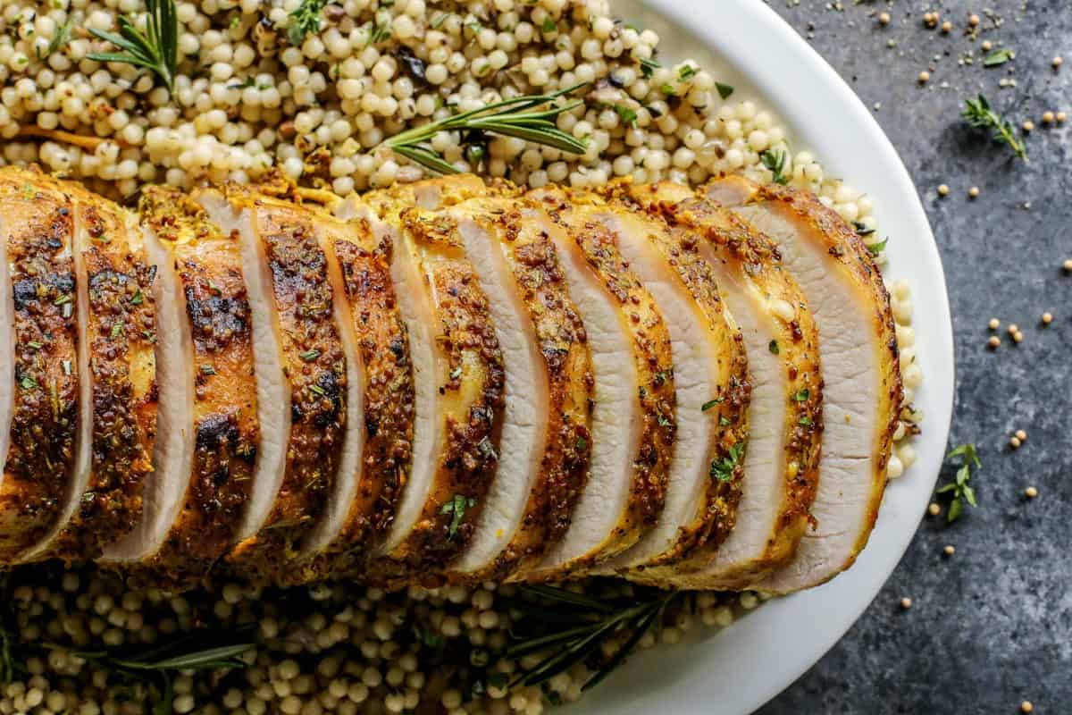 This pork loin roast recipe is juicy and tender, slathered with a savory mustard mixture and oven-roasted for a satisfying, easy pork dinner. Overhead view of sliced mustard pork loin roast over a bed of pearl couscous.
