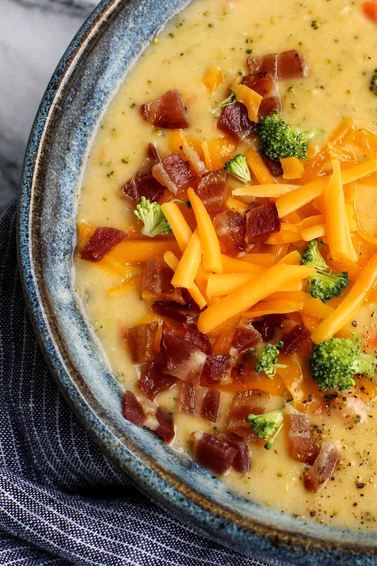 Extra cheesy and creamy, this broccoli cheddar soup recipe is loaded with all kinds of wholesome veggies. Don't forget a sprinkle of bacon! Overhead close up view of a bowl of broccoli cheddar soup garnished with crumbled bacon and shredded cheese.