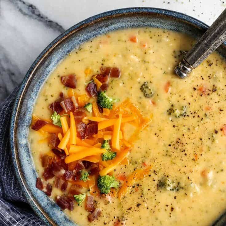 Overhead view of a bowl of broccoli cheddar soup garnished with crumbled bacon and shredded cheese.