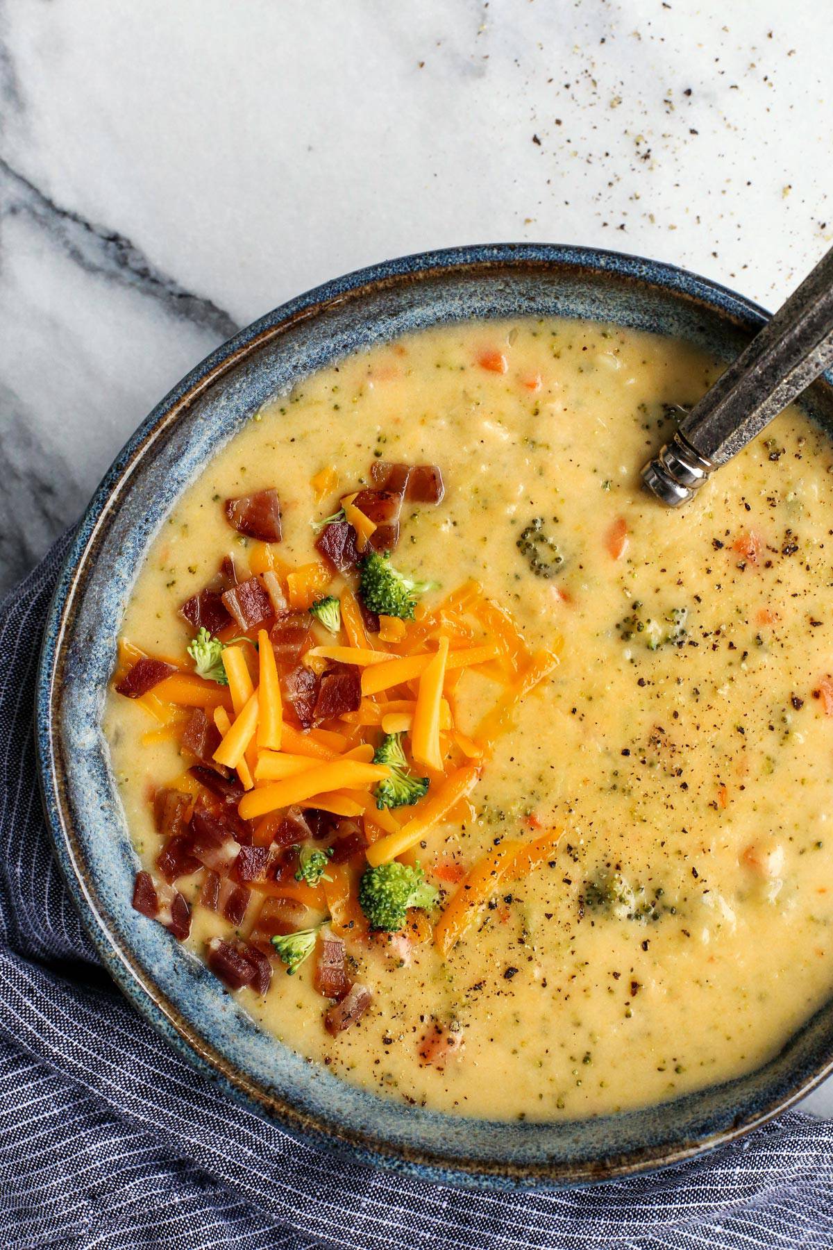 Extra cheesy and creamy, this broccoli cheddar soup recipe is loaded with all kinds of wholesome veggies. Don't forget a sprinkle of bacon! Overhead view of a bowl of broccoli cheddar soup garnished with crumbled bacon and shredded cheese.